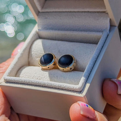 9 Carat Gold Stud Earrings with Pirate/Black Sea Glass and Bubble Design in an ivory plush jewellery box held by hand above shimmering ocean by Booblinka Jewellery