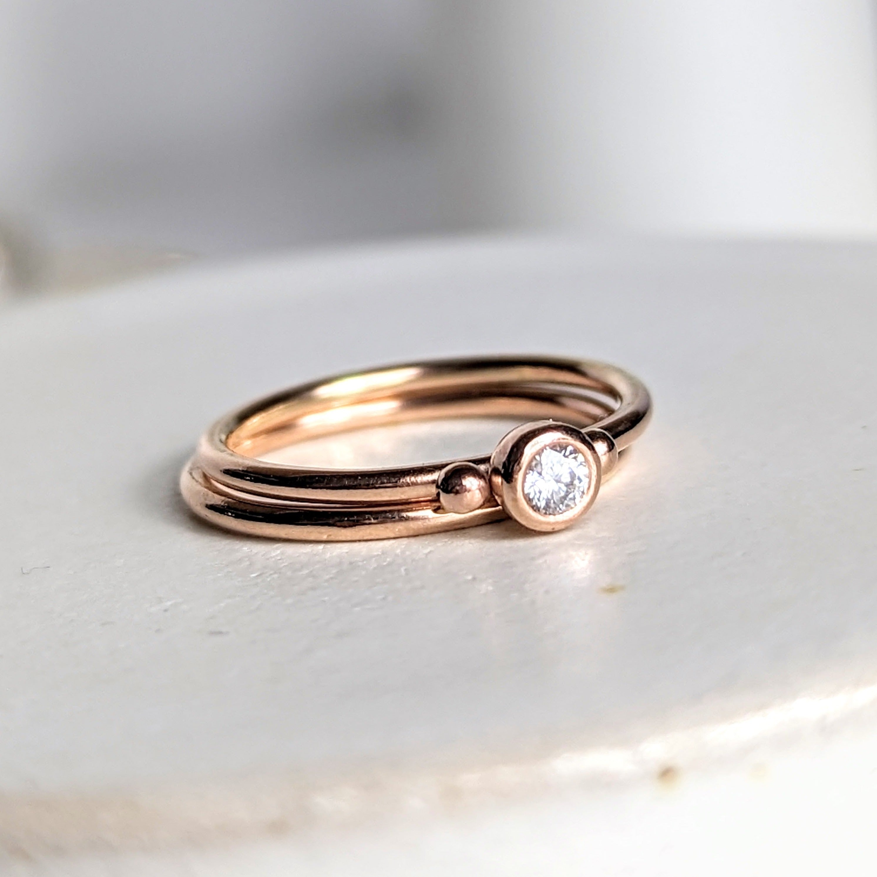 Dainty rose gold stacking rings with sparkly moissanite DEI collection on white background 