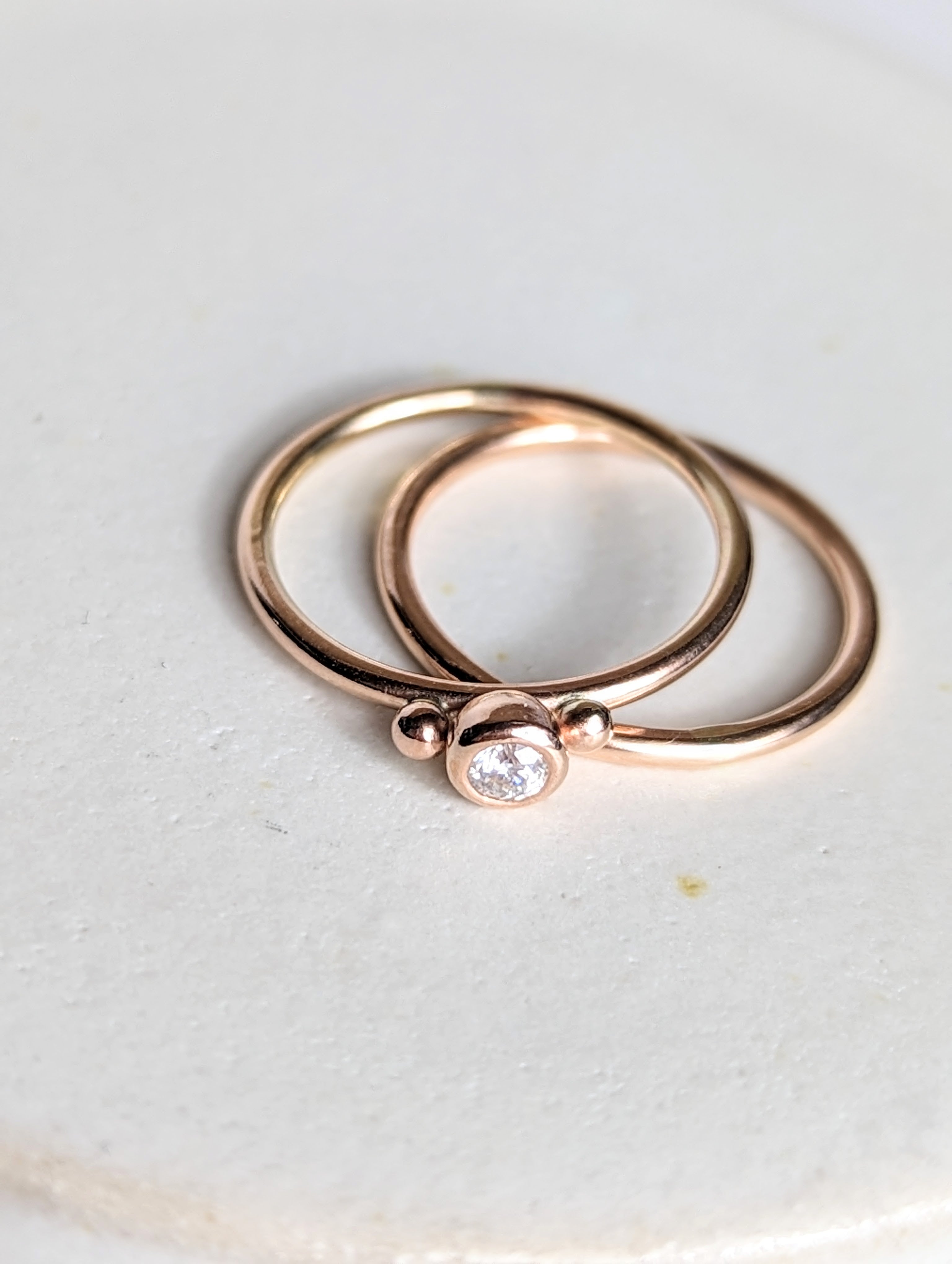 Dainty rose gold stacking rings with sparkly moissanite DEI collection on white background top view