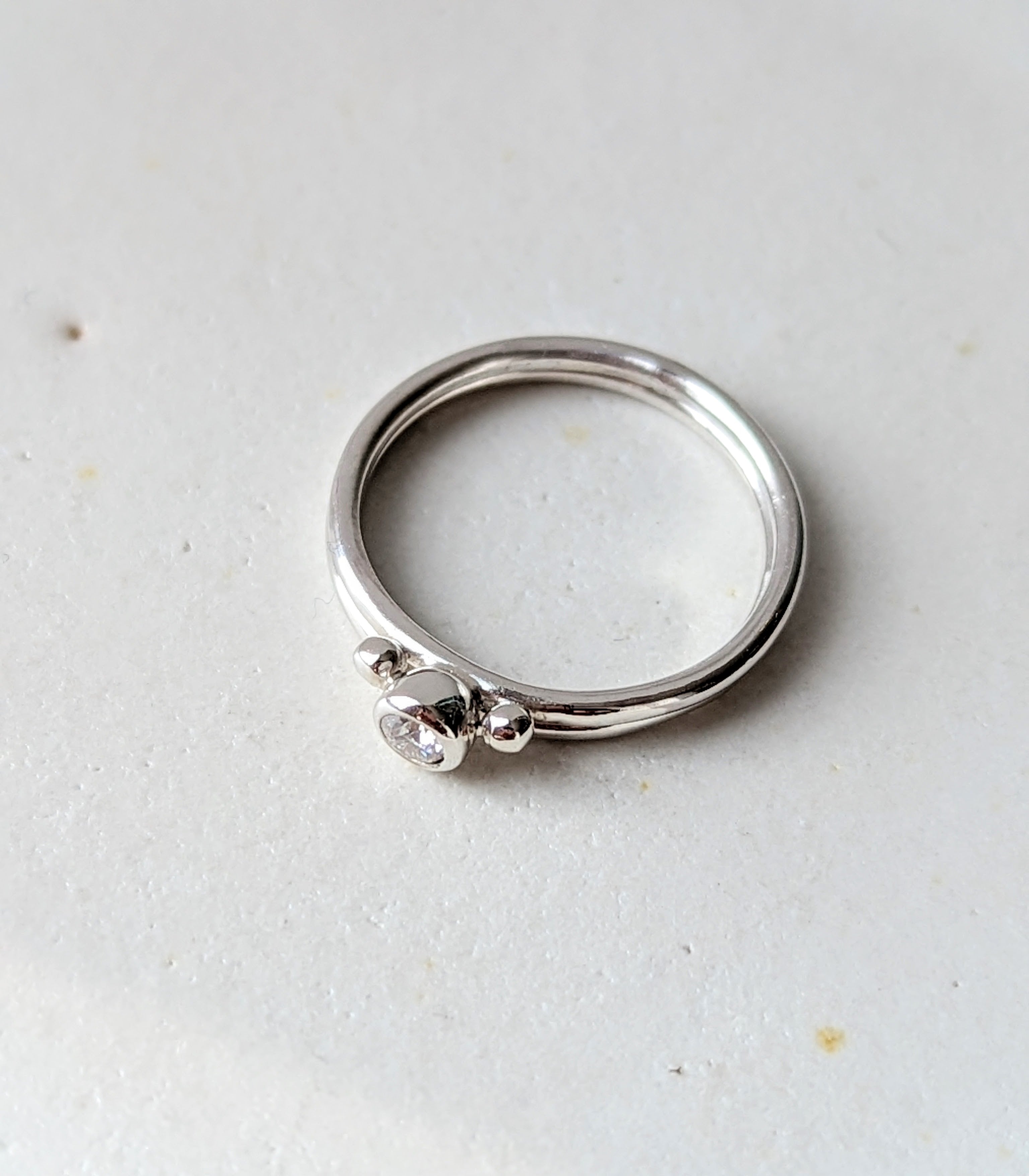 Silver minimalistic stacking rings with sparkly moissanite and two granules on white background Dei Collection top view