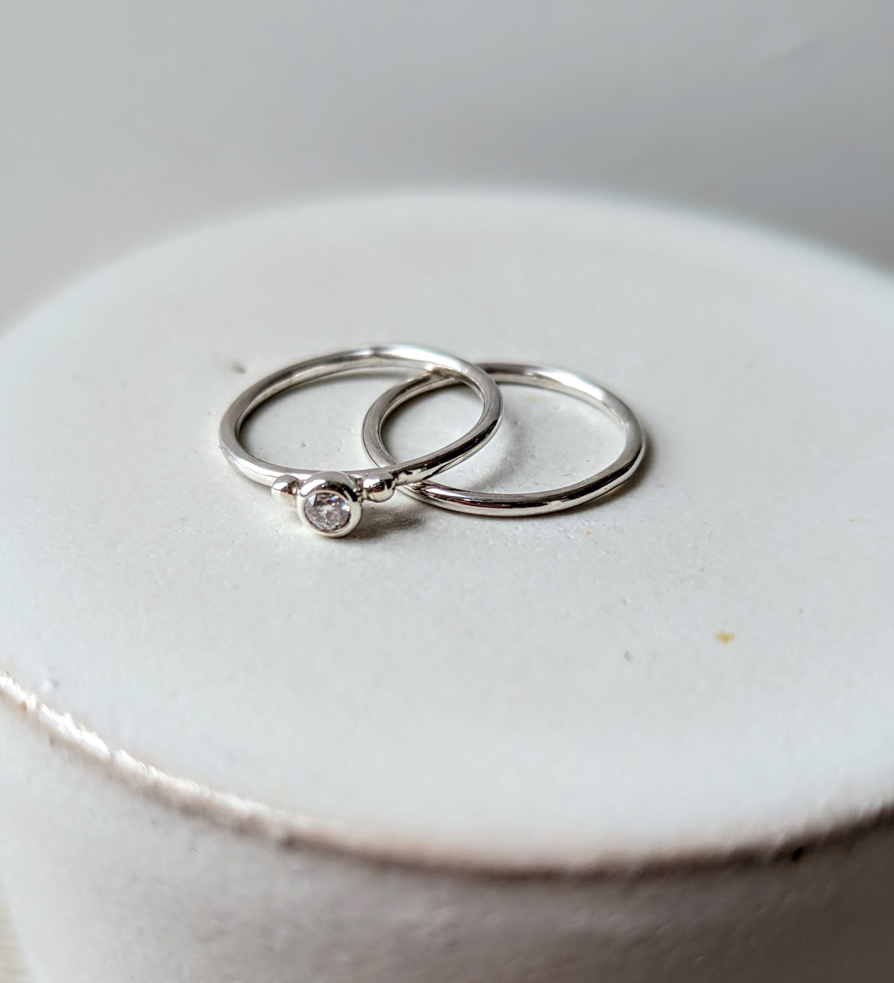 Silver minimalistic stacking rings with sparkly moissanite and two granules on white background Dei Collection