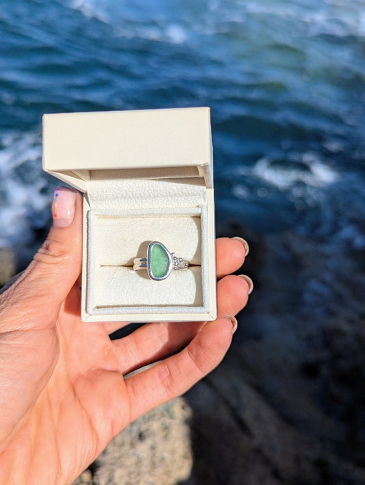 Pastel Green Sea Glass Silver Ring with Bubble Details  from Allure Collection in an ivory jewellery box held by hand above the ocean by Booblinka Jewellery