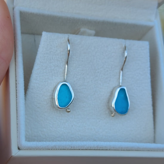 Turquoise Sea Glass Silver Drop Earrings held by hand above the ocean, capturing the vibrant turquoise hues and coastal charm.