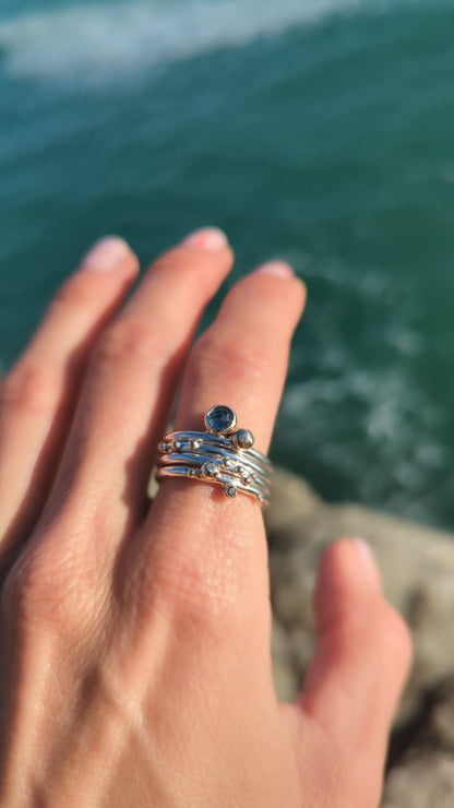 London Blue Topaz and Diamonds Stacker Rings on a finger above the ocean