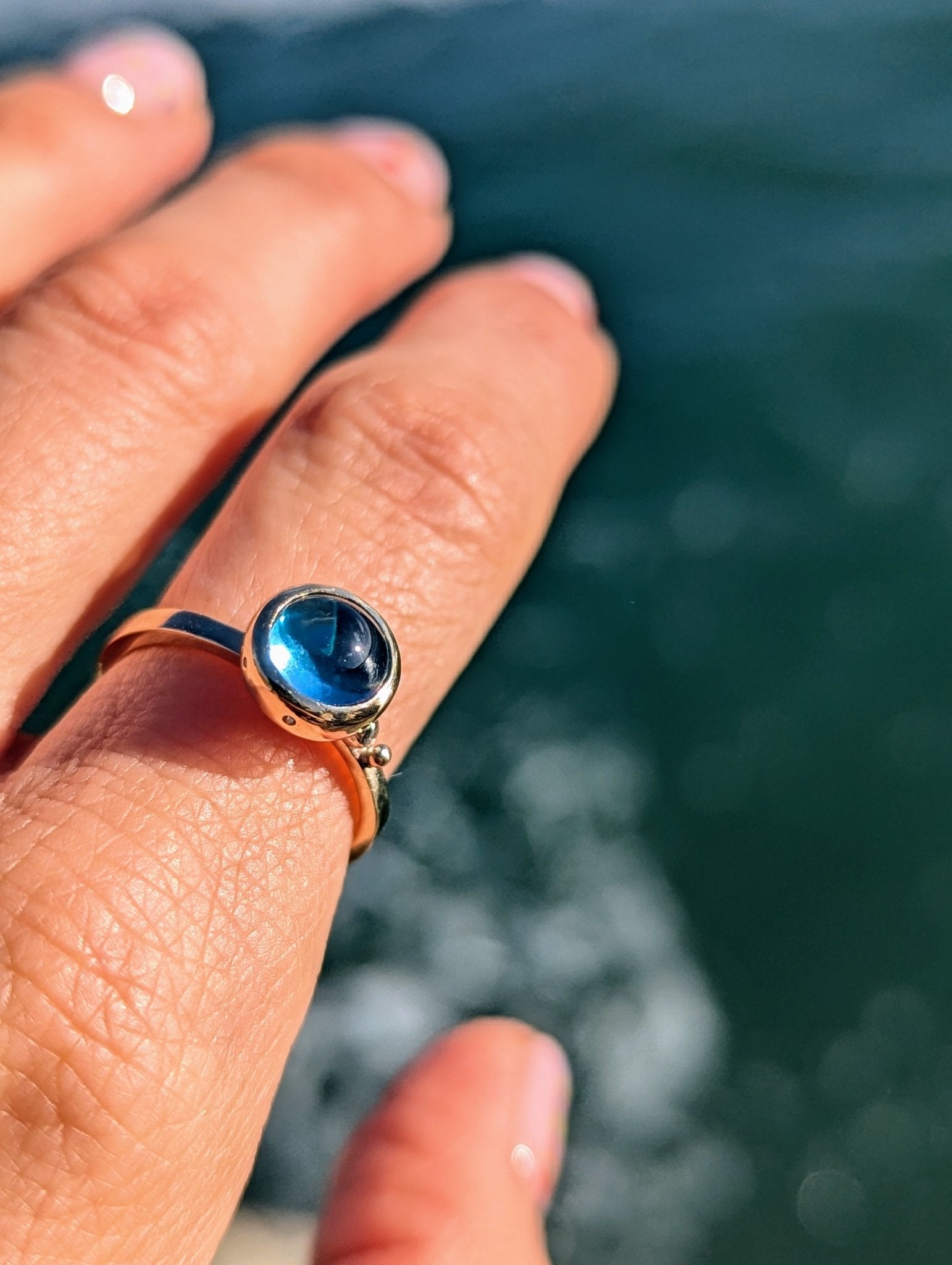 Swiss Blue Topaz Cabochon Gold Ring with diamond from Drop of the Ocean Collection worn on a hand above the Atlantic ocean made by Booblinka Jewellery