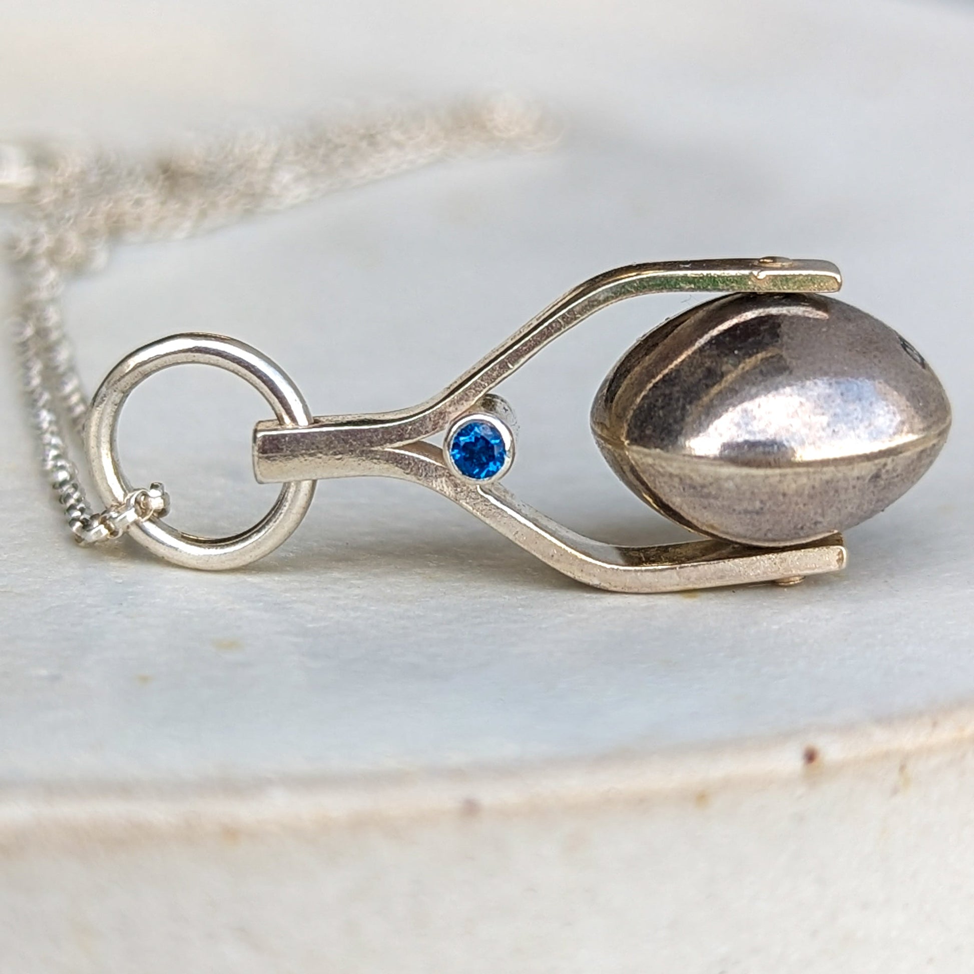 Detailed shot of the spinning moon necklace in sterling silver with a blue gemstone, showcasing its unique design as seen in 'Playing Nicely' by Booblinka Jewellery 